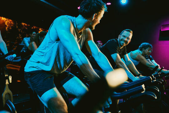 Friends enjoying a high-energy indoor cycling spin class for fitness and motivation in a neon-lit studio