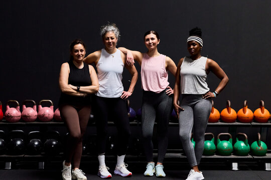 Four women in gym posing with kettlebells showing fitness, strength and diverse teamwork and empowerment