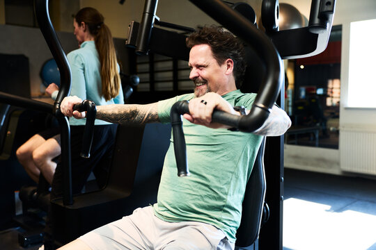 Man pushing chest-press machine at gym during an intense strength training session and smiling with effort