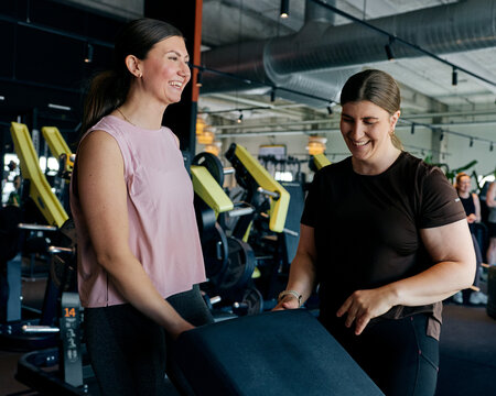 Two friends smiling during a gym workout session while adjusting equipment and training together