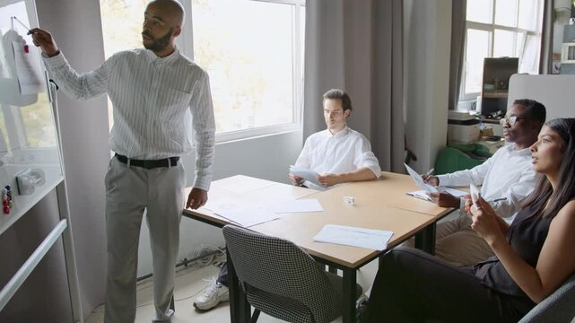 A group of four people engage in a meeting, sharing ideas and reviewing project details in an office setting. The atmosphere is collaborative as they focus on teamwork and discussion