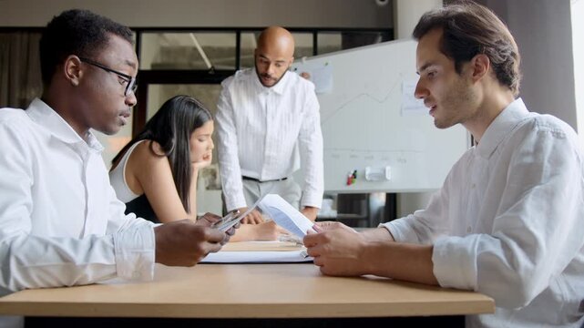 Four diverse colleagues discuss about contract details and data at an office table and work together to solve problems and make decisions to reach a common goal