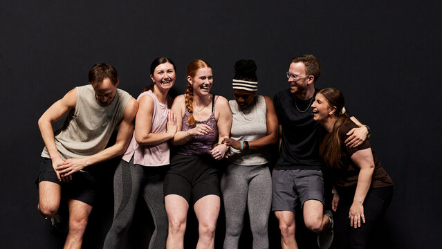 Smiling diverse group of friends enjoying a casual group workout and fitness session together. They stand side by side, with a good atmosphere between them. Smiling and laughing.