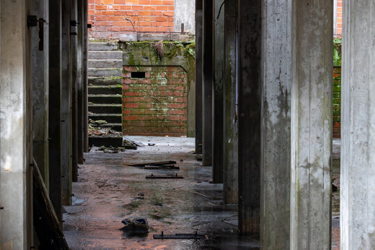 La Tuque, Quebec, 16 May 2026 : Concrete pillars line a wet, decaying floor inside an abandoned building with crumbling brick walls and stairs.