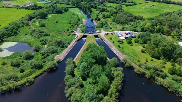 High angle aerial drone view of a scenic forked canal junction for narrowboats surrounded by blue leisure lakes and a green rural landscape in Kingsbury Warwickshire UK