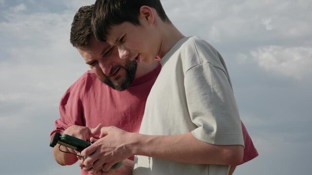 Father Teaching Son How to Operate a Drone with a Remote Controller Outdoors