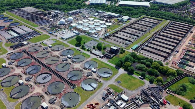 Drone perspective looking down at circular primary sedimentation tanks, final settlement clarifiers, and massive anaerobic digestion domes at the Minworth wastewater treatment facility near Birmingham