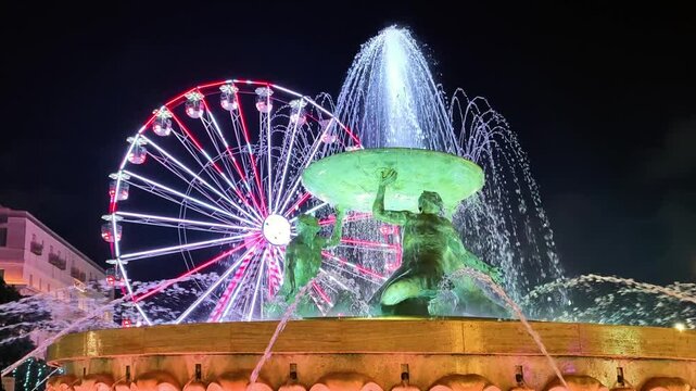 Valletta, Malta, illuminated Triton fountain with Ferris wheel in background at night