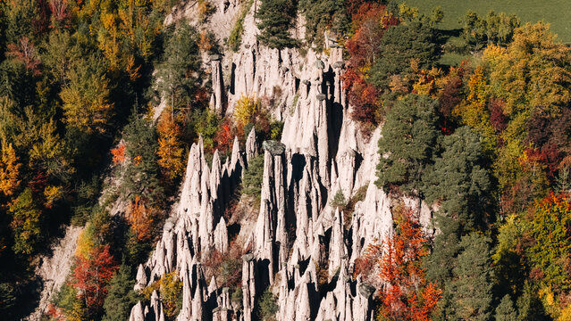 Aerial view of the Piramidi di Terra di Longomoso hoodoos surrounded by vibrant autumn foliage and dense forest in Ritten, Trentino-Alto Adige, Italy.