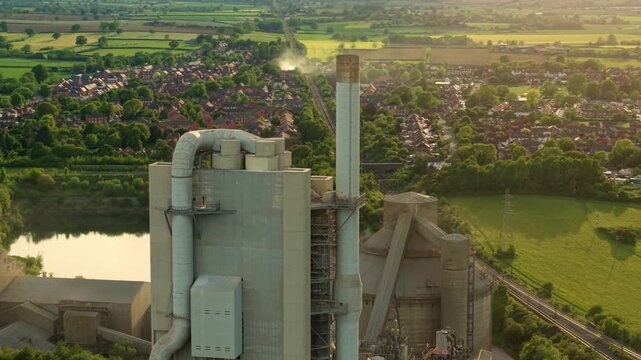 Drone shot of Rugby Cement Plant industrial manufacturing facility and tall exhaust stacks during a vibrant sunset in England