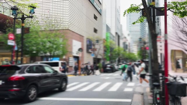 Busy pedestrian crosswalk in the Ginza district of Tokyo. People and cyclists crossing the street near modern buildings. Impressive skyscrapers rise into the sky over the city traffic. 