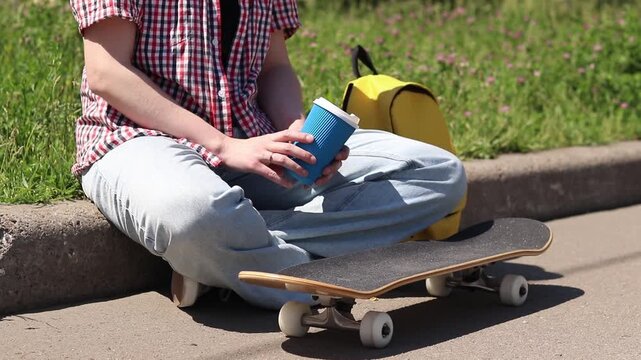 Unrecognizable person in comfortable summer clothes with skateboard. Young girl resting on the side of the road with skateboard. Concept of youth culture, sports and recreation