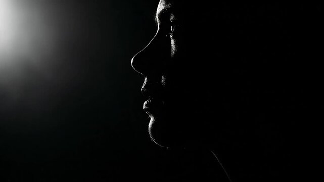 Silhouette of a face in profile against a dark background with dramatic lighting.