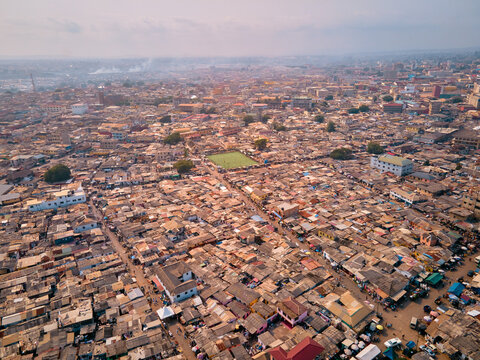 Aerial view of James Town featuring dense residential rooftops and a green football pitch under a hazy sky in Accra, Greater Accra Region, Ghana.