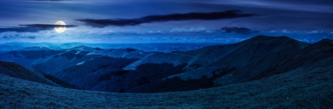 beautiful panorama of mountainous landscape at night. full moon over wide view of cloudy sky over the grassy slope of a mountain ridge. mysterious summer weather. adventure tourism in highland