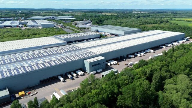 High angle drone view of a major logistics fulfillment center with commercial freight trucks docked at distribution bays.