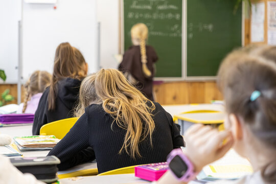 Elementary school students sit at desks in a classroom, focusing on their studies as a classmate writes on the blackboard, representing the academic environment of primary education