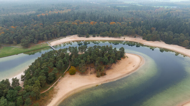 Aerial view of Henschotermeer lake featuring a central island and sandy beaches surrounded by a dense pine forest in Woudenberg, Utrecht, Netherlands.
