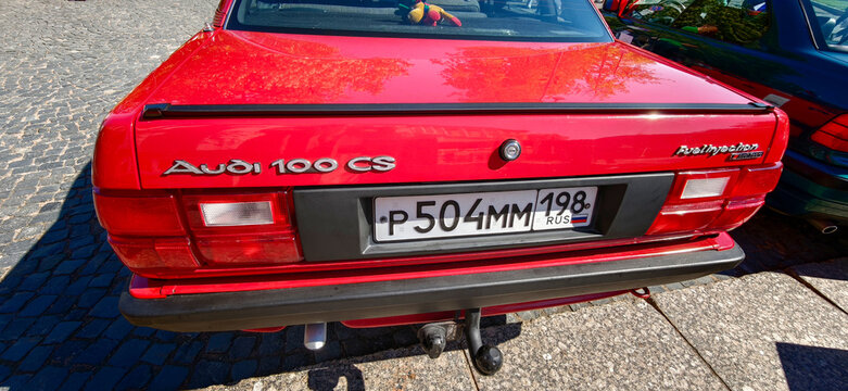 Saint Petersburg, Russia - May 23, 2026: Red Audi 100 CS rear view showcasing distinctive badge and license plate on a cobblestone street with greenery in the background