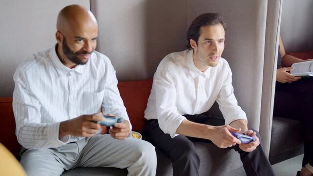 In the office lounge, diverse colleagues gather for a fun break. They play video games on consoles, sharing laughter and friendly rivalry, building connections over smiles and cheers