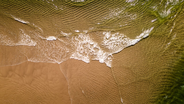 Drone shot of ocean waves washing on golden sand texture