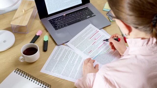Female editor correcting text on paper with marker near laptop. Professional woman doing document translation and proofreading work at office desk.
