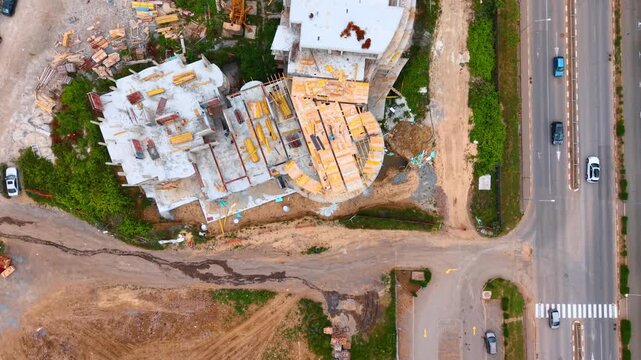 Aerial top view of building under construction next to road. Top-down aerial shot of residential concrete building structure with timber formwork next to asphalt road.