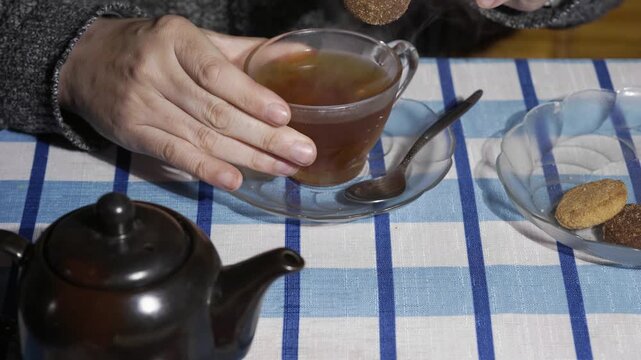 Close-up of hands dunking a chocolate biscuit into steaming tea and taking a sip