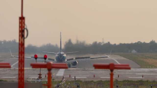 Rear view of a commercial passenger airplane landing and braking on the runway. Jetliner slowing down with deployed spoilers on the tarmac behind runway lights. Heat haze from the engine.