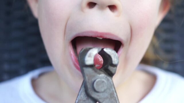 A humorous close-up of a child with missing teeth making a joke, bringing a pair of old construction pliers to his open mouth as if to pull out a tooth.