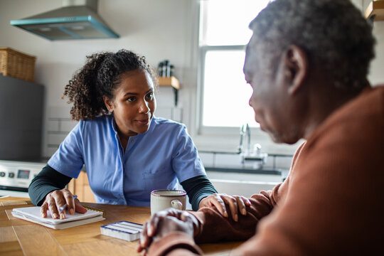 Home caregiver comforting senior patient at kitchen table
