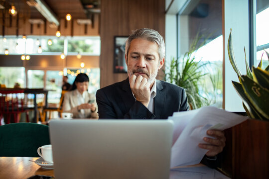 Mature businessman reviewing documents on laptop in cafe