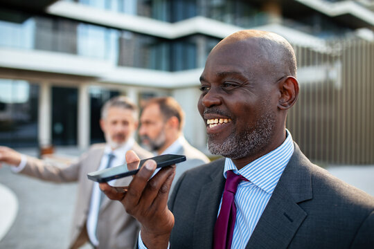 Smiling businessman using voice assistant outside modern office building