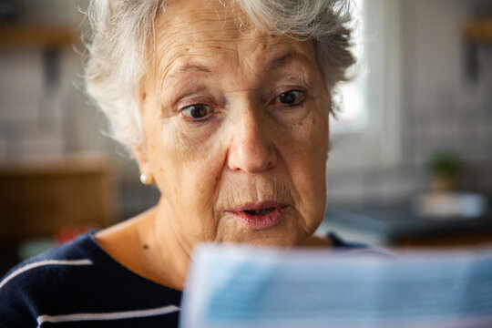 Senior woman surprised by household bill at home kitchen