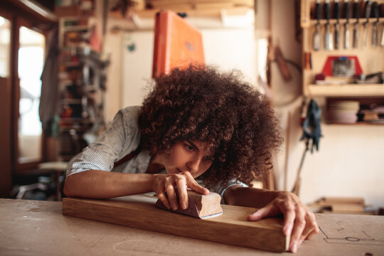 Woman sanding wooden plank in carpentry workshop