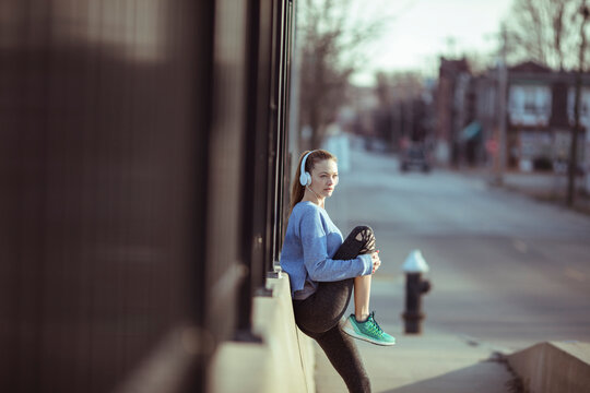 Young woman runner with headphones resting on urban sidewalk