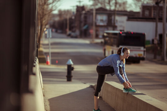 Young woman runner tying shoe on urban sidewalk
