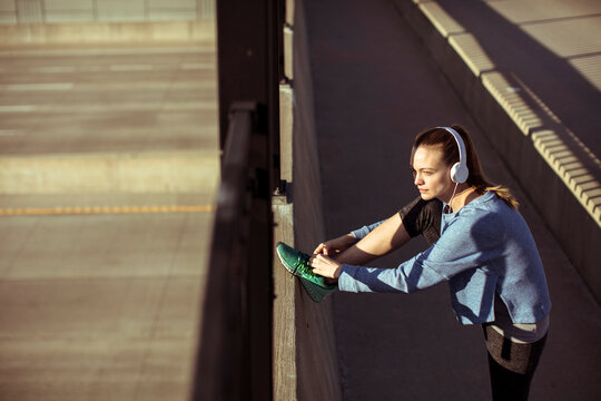Young woman stretching with headphones on urban bridge