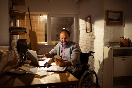 Middle-aged man in a wheelchair video calling from home office at night