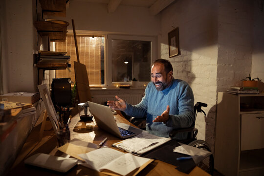 Smiling man in wheelchair on video call at home office at night