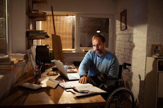 Man in wheelchair working late at home office with laptop