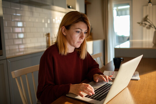 Woman working on laptop at kitchen table at home
