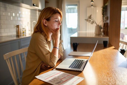Worried woman paying bills online at home kitchen table