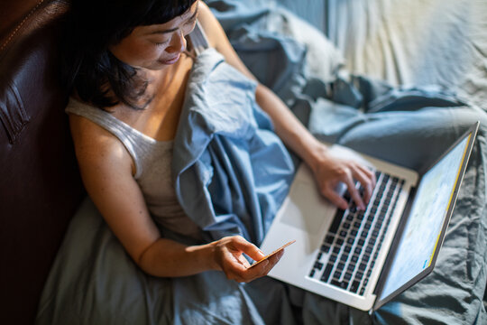 Woman shopping online with credit card in bed at home