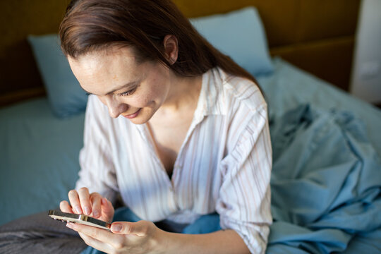 Smiling woman using smartphone in bed at home