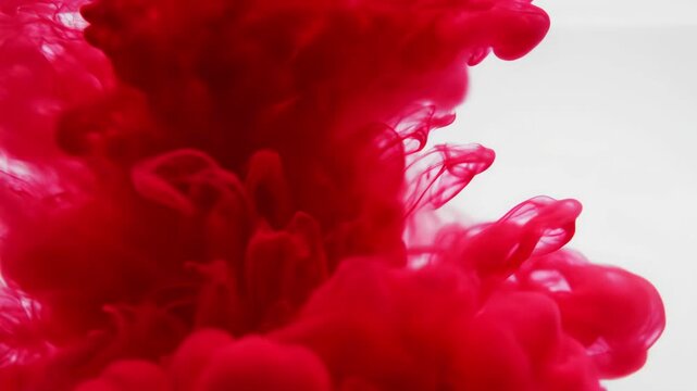 Red pigment spreading through clear liquid forming dramatic abstract clouds, fluid ink diffusion creating organic shapes and swirling motion against clean background with vivid artistic energy
