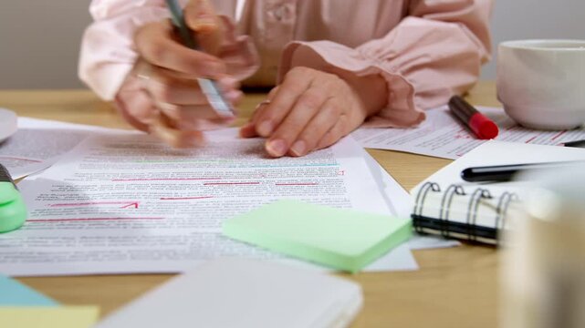 Female editor correcting text on paper with marker near laptop. Professional woman doing document translation and proofreading work at office desk.