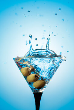 A green olives drops into a martini glass, creating a beautiful splash.