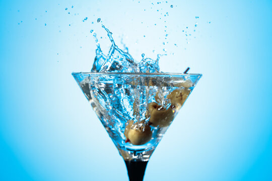 A green olives drops into a martini glass, creating a beautiful splash.