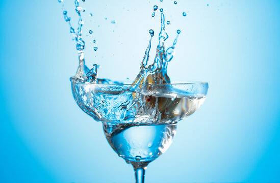 A green olives drops into a martini glass, creating a beautiful splash.